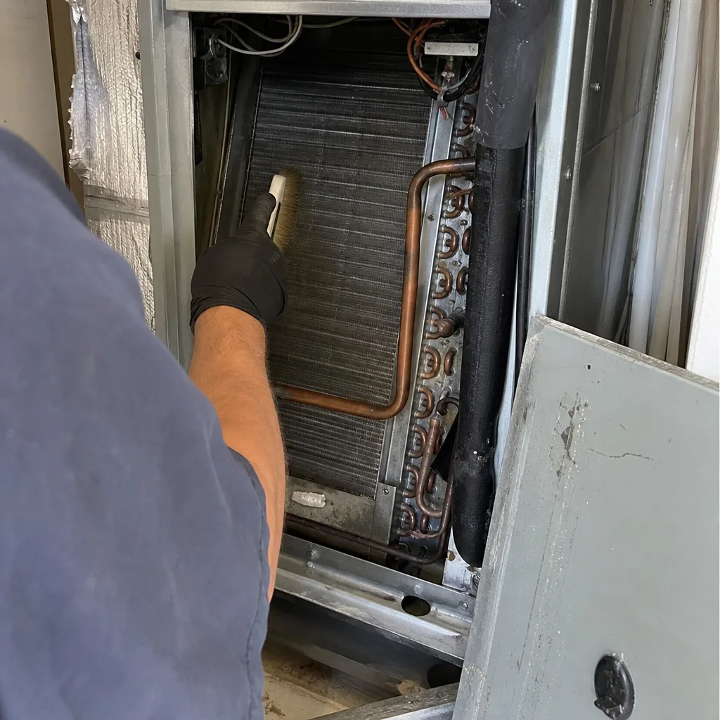 Technician cleaning HVAC evaporator coils with a brush for maintenance